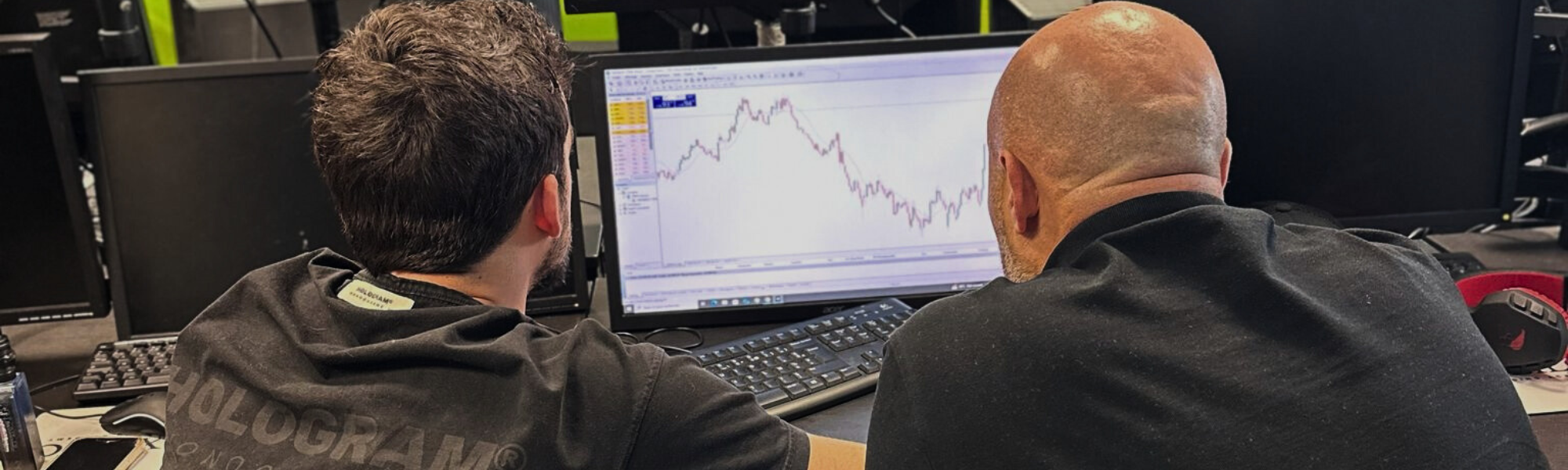 Un homme en costume observe un écran rempli de graphiques de trading et de taux de change forex, hésitant entre acheter et vendre.