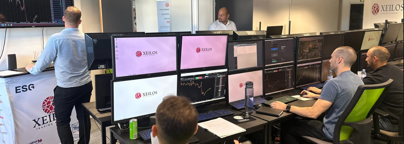 Salle des marchés de Xeilos Trading Academy avec plusieurs écrans de trading et des élèves en formation devant leurs postes.